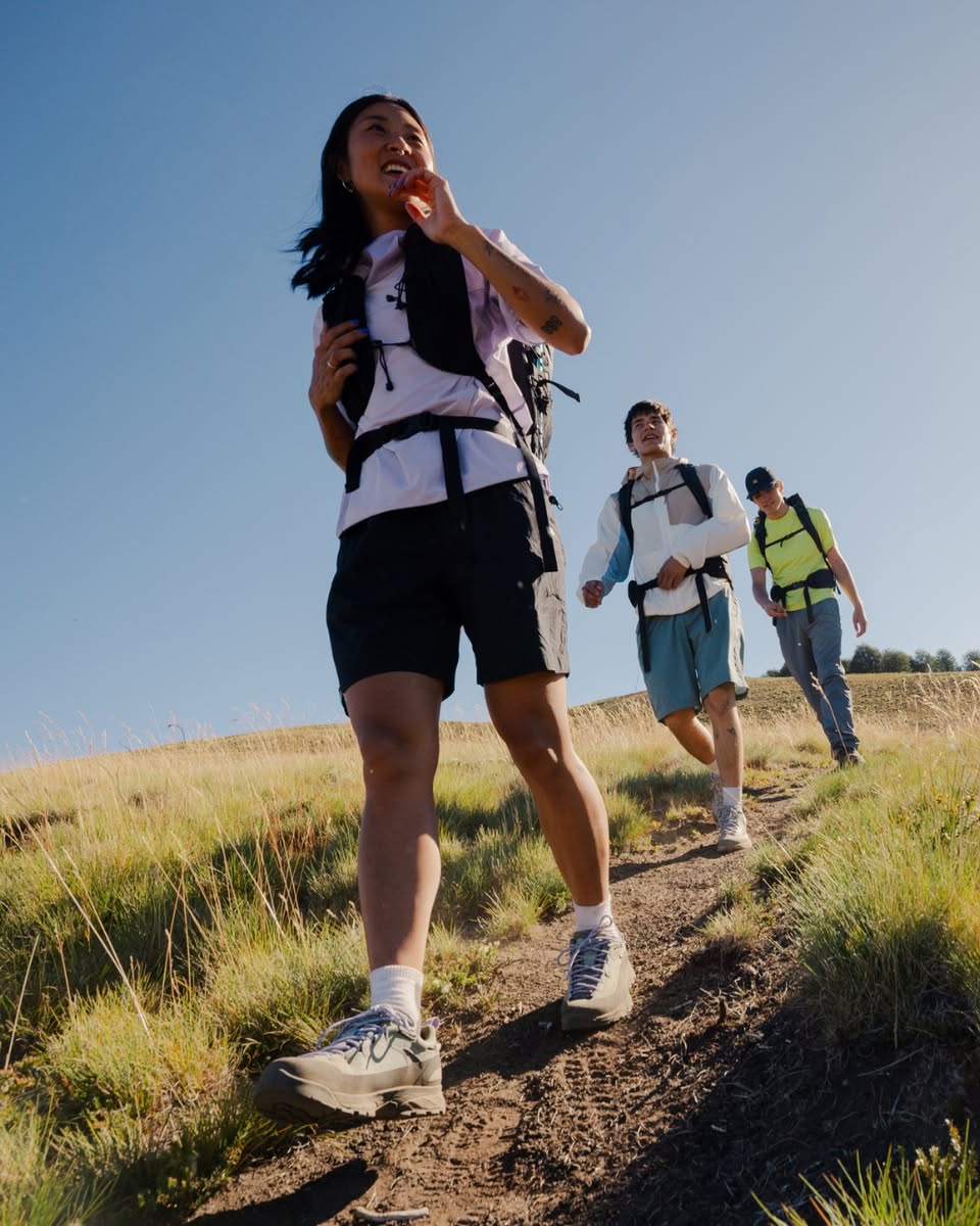 Three hikers ascending a grassy hill under a clear blue sky