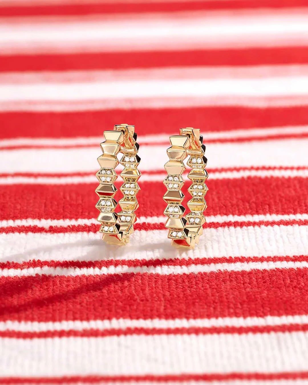 APM Monaco gold hoop earrings on striped fabric