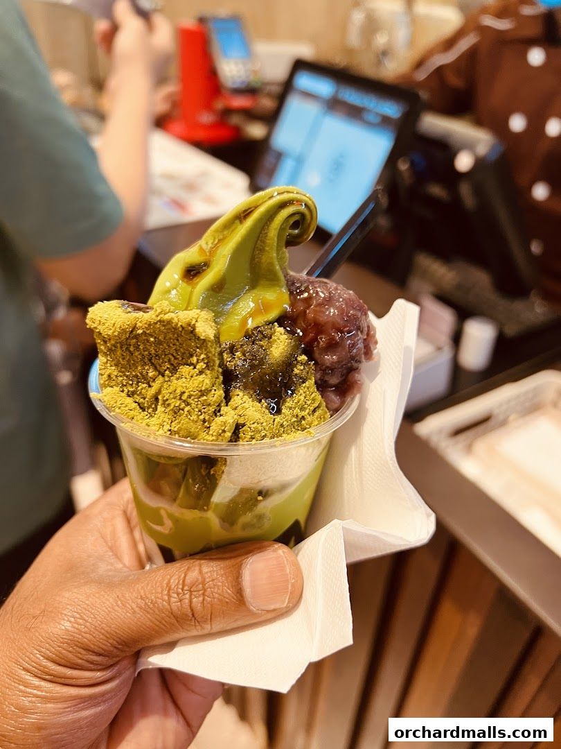 A hand holds a delicious matcha dessert with red bean paste and crumble topping.