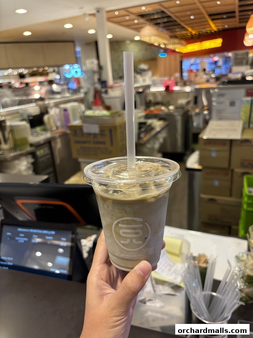 A hand holds a matcha latte from 108 Matcha Saro in front of the shop's counter.