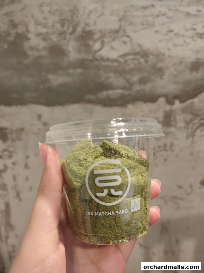 A hand holds a clear cup filled with green matcha mochi dusted with matcha powder.
