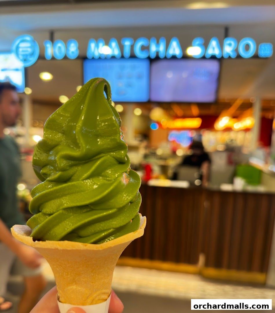 A hand holds a vibrant green matcha soft serve ice cream cone in front of the shop.
