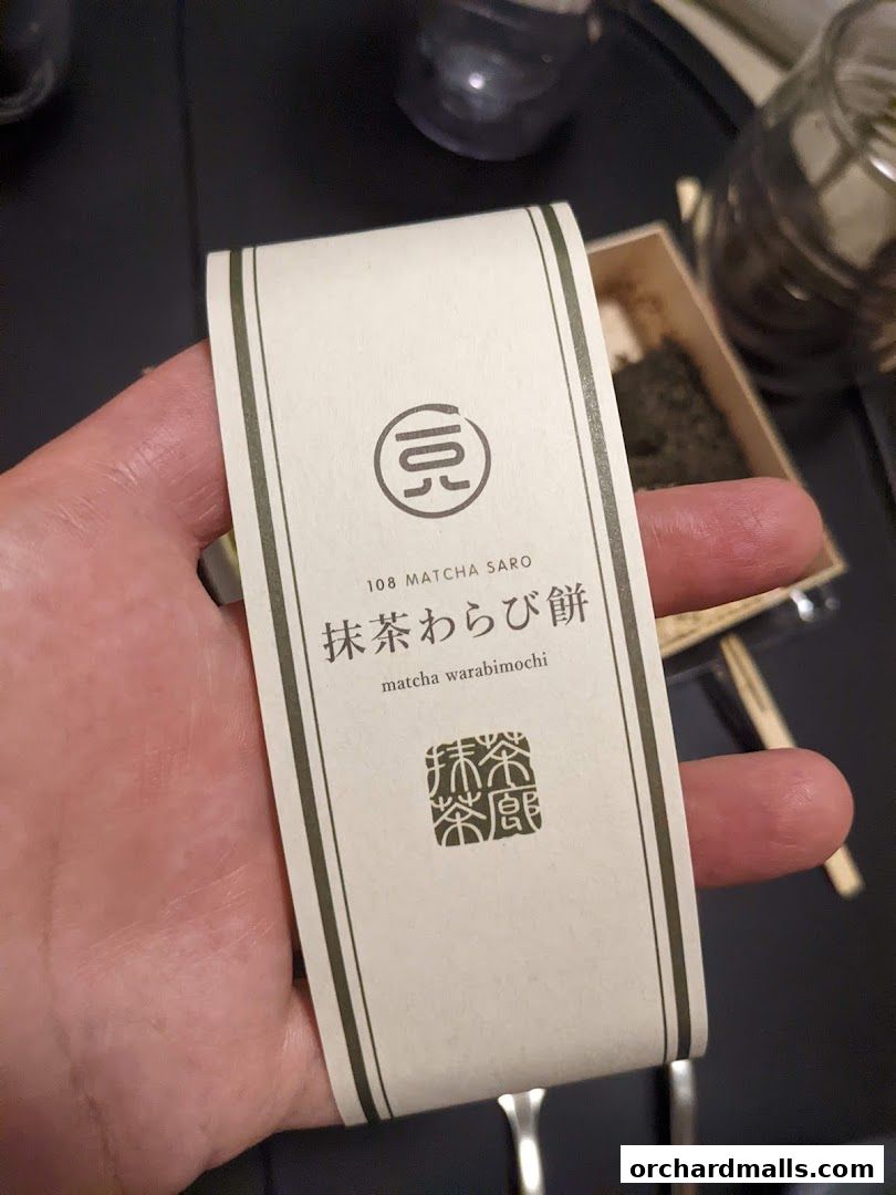 A hand holds a paper sleeve for matcha warabimochi from 108 Matcha Saro.