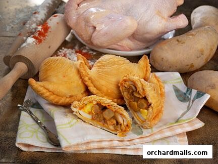 A close-up of crispy curry puffs with chicken and potato filling, alongside ingredients.