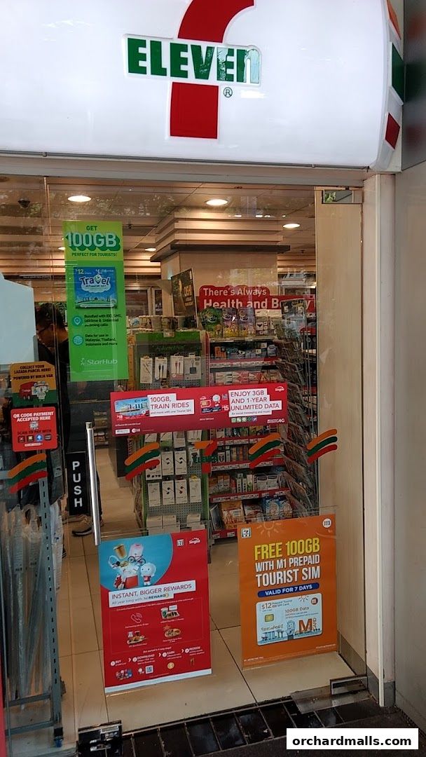 The entrance of a 7-Eleven convenience store with promotional posters displayed.