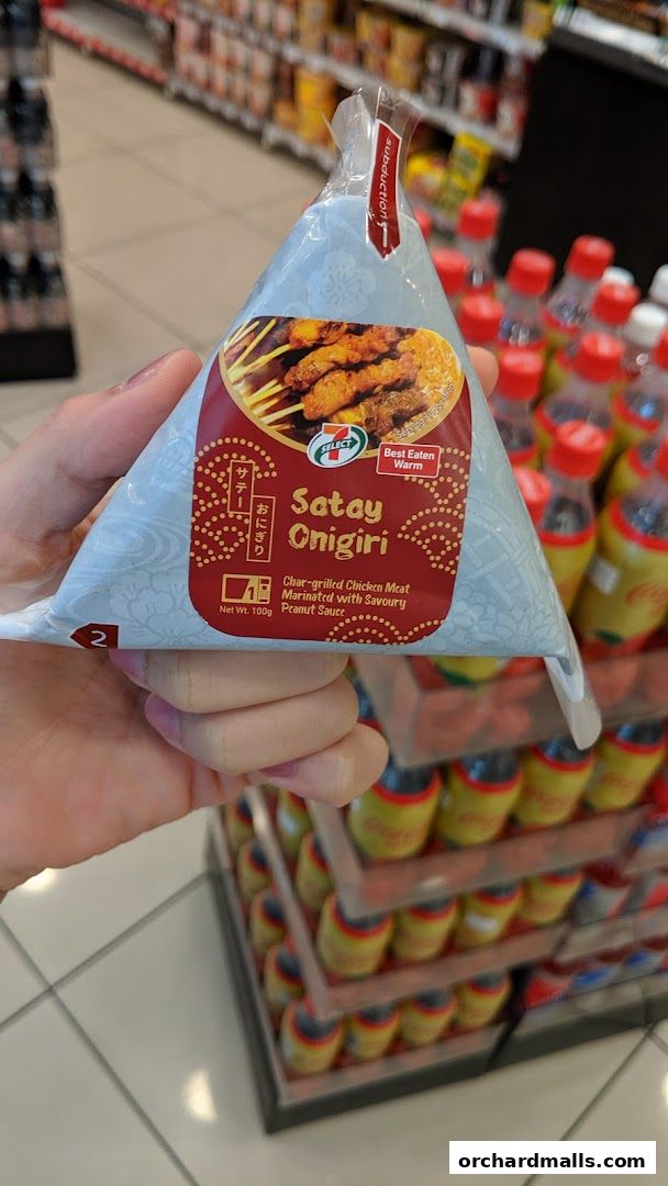 A hand holds a packaged Satay Onigiri with char-grilled chicken and peanut sauce.