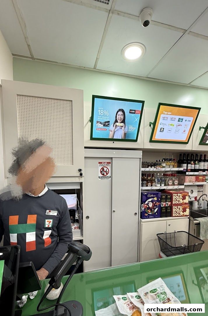 A 7-Eleven store interior showing a cashier, shelves with products, and digital displays.