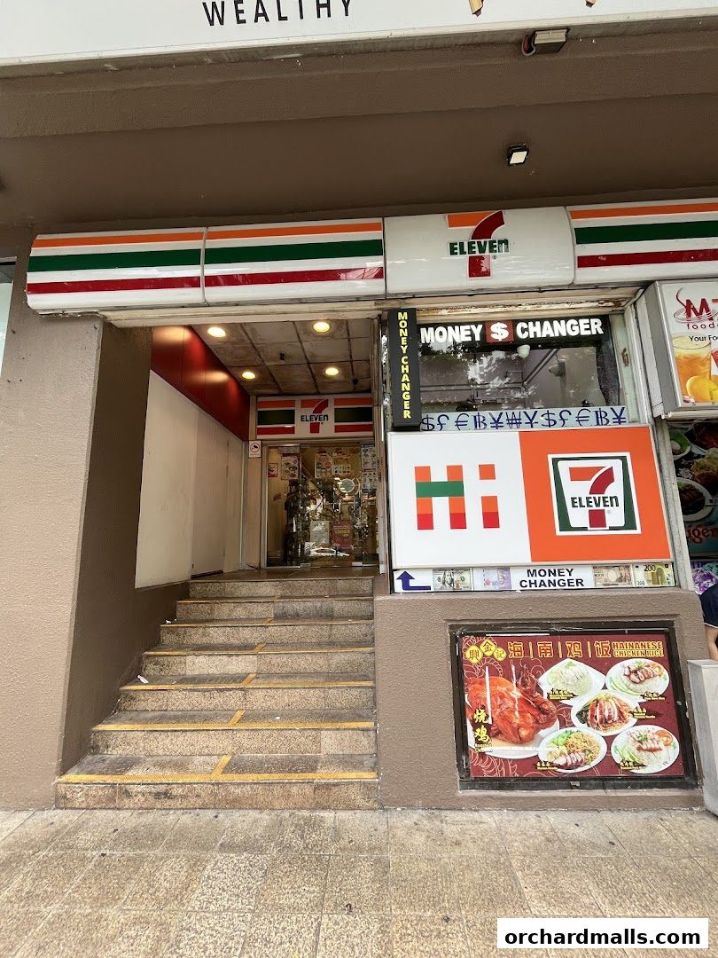 The exterior of a 7-Eleven convenience store with a money changer and food advertisements.