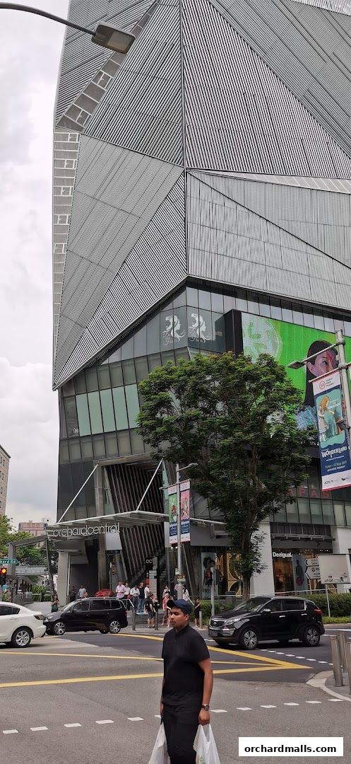 A man walks across a street in front of a modern building with a large digital billboard.
