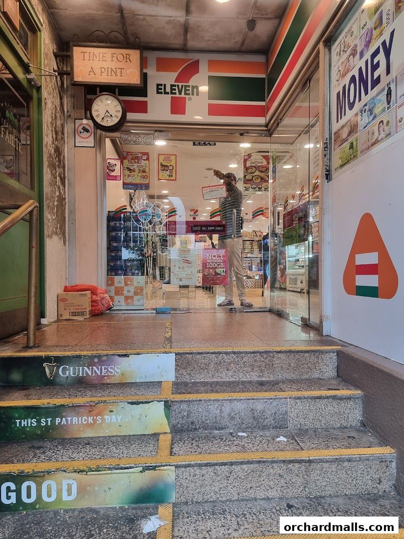 The entrance to a 7-Eleven convenience store with promotional signs and a clock.