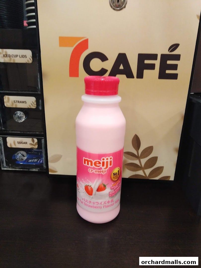 A bottle of Meiji strawberry flavored milk in front of a 7-Eleven cafe machine.