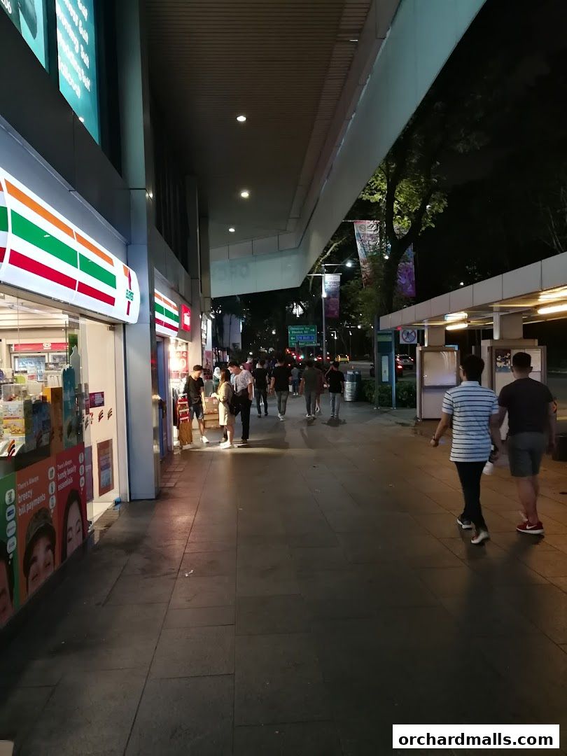 A 7-Eleven store front at night with people walking on the sidewalk.