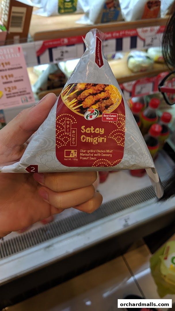 A hand holds a 7-Eleven Satay Onigiri with char-grilled chicken meat and peanut sauce.