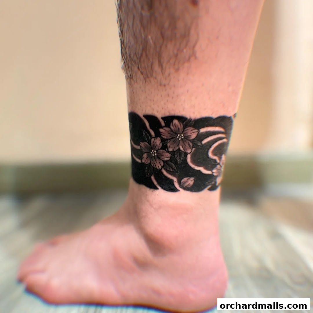 A close-up of a black floral tattoo band around a person's ankle.