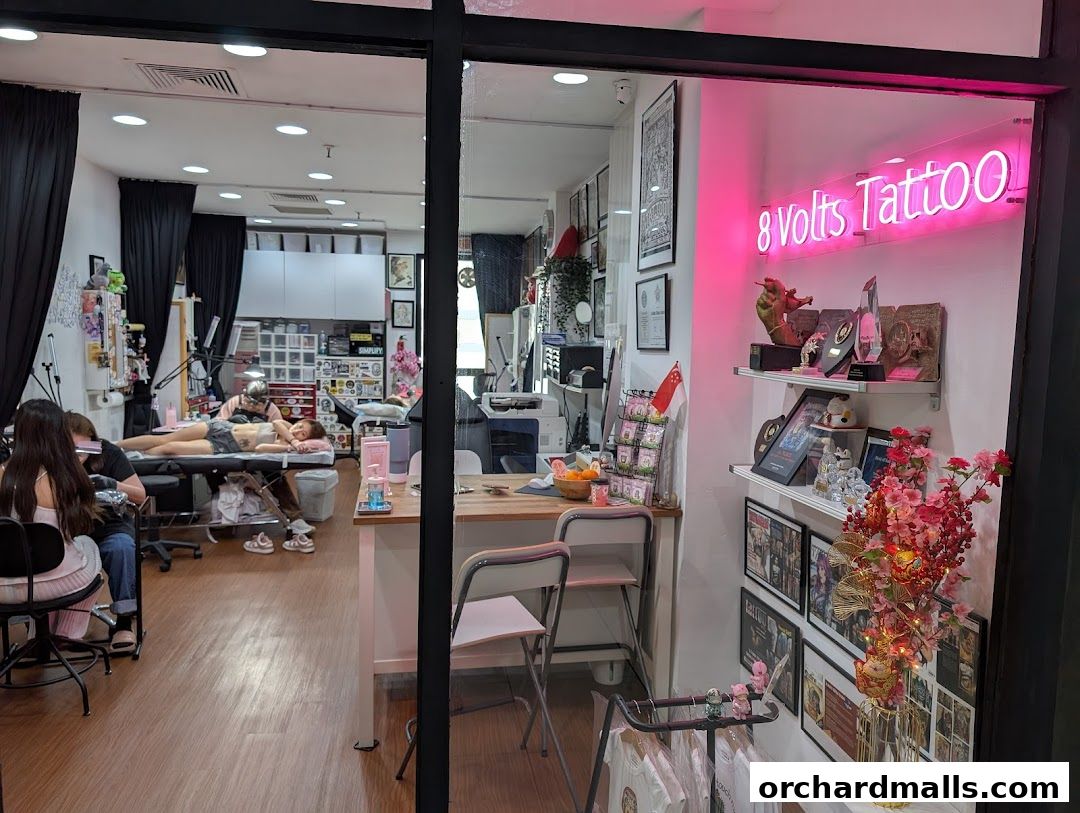 Interior view of 8 Volts Tattoo shop with artists tattooing clients and neon sign.