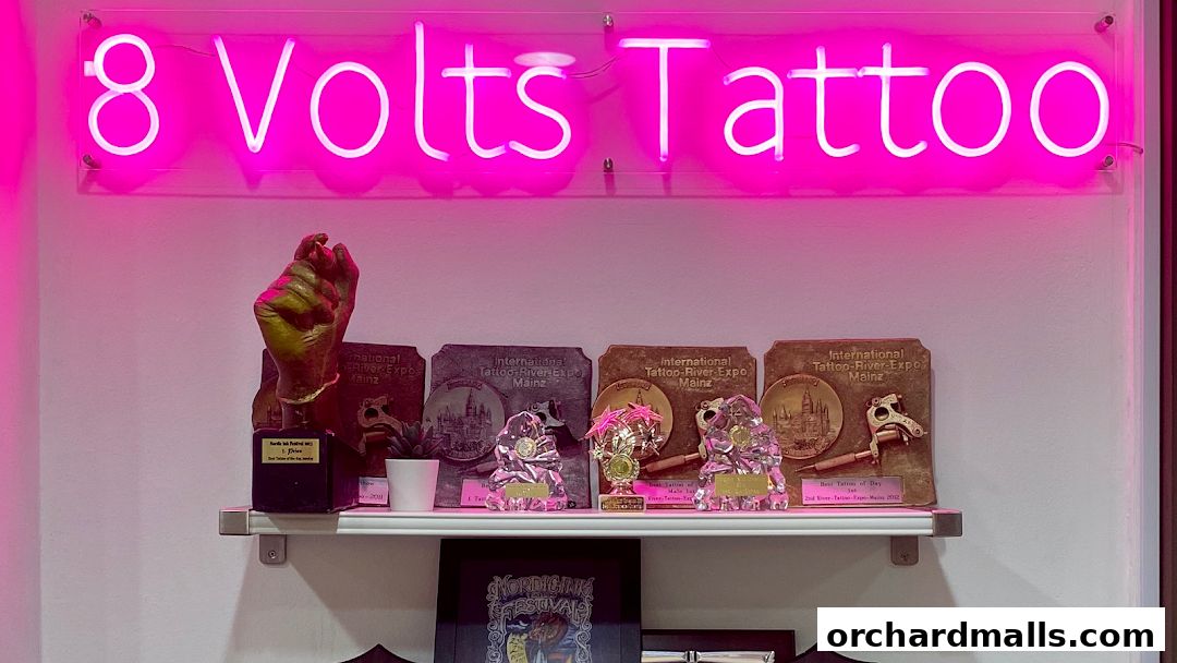 Neon sign '8 Volts Tattoo' above a shelf displaying awards and trophies.