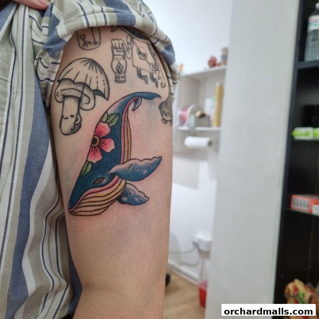A person's arm displays a colorful whale tattoo with flowers and other designs.