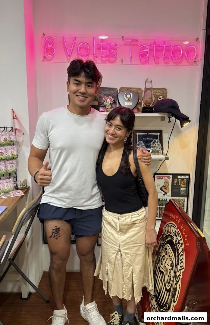 A couple poses in front of the 8 Volts Tattoo shop sign and display.