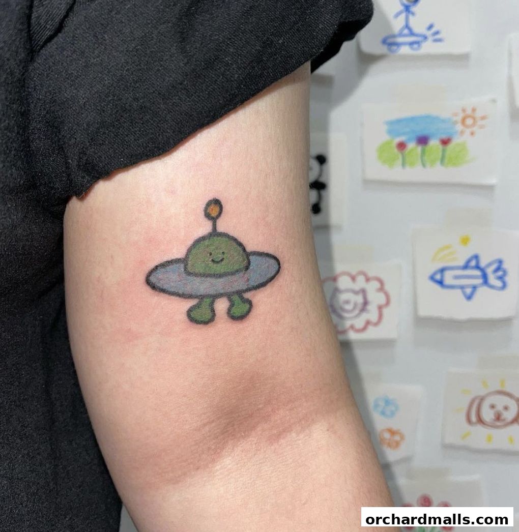 A close-up of a cute alien spaceship tattoo on an arm, with artwork on the wall behind.