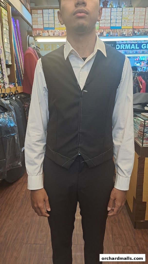 A person models a black vest over a white shirt and black pants at a tailor shop.