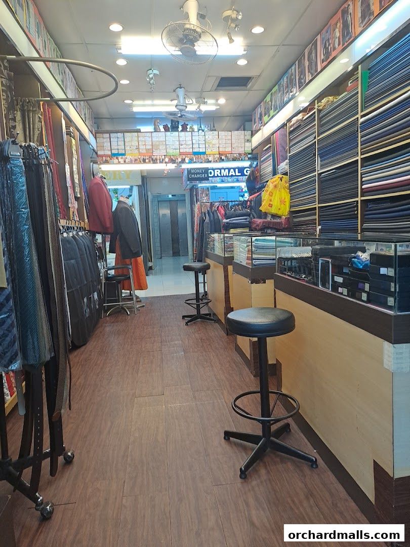 Interior view of a tailor shop with fabric rolls, suits, and accessories displayed.