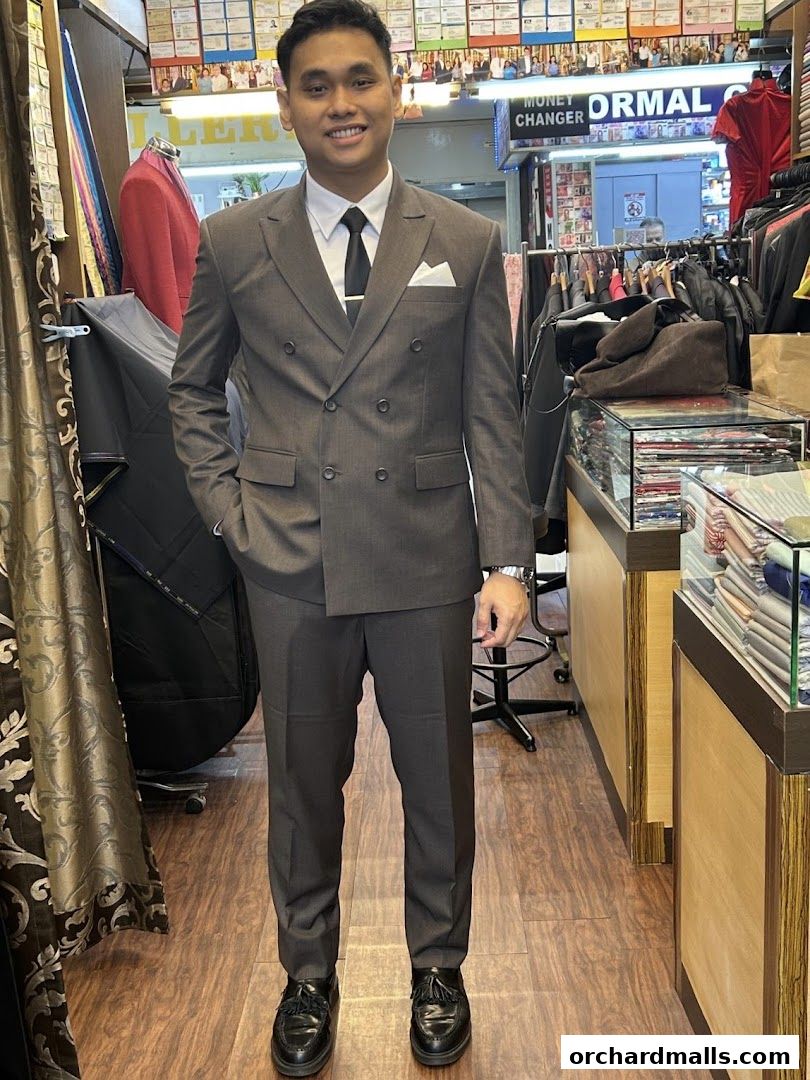 A man models a custom-tailored grey suit inside a tailor shop.