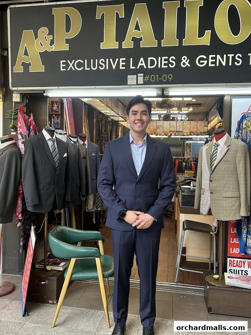 A man in a navy suit stands in front of AP Custom Tailors, showcasing their exclusive tailoring services.