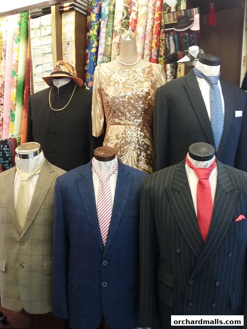 Mannequins display tailored suits and a sequined dress with colorful fabrics in the background.