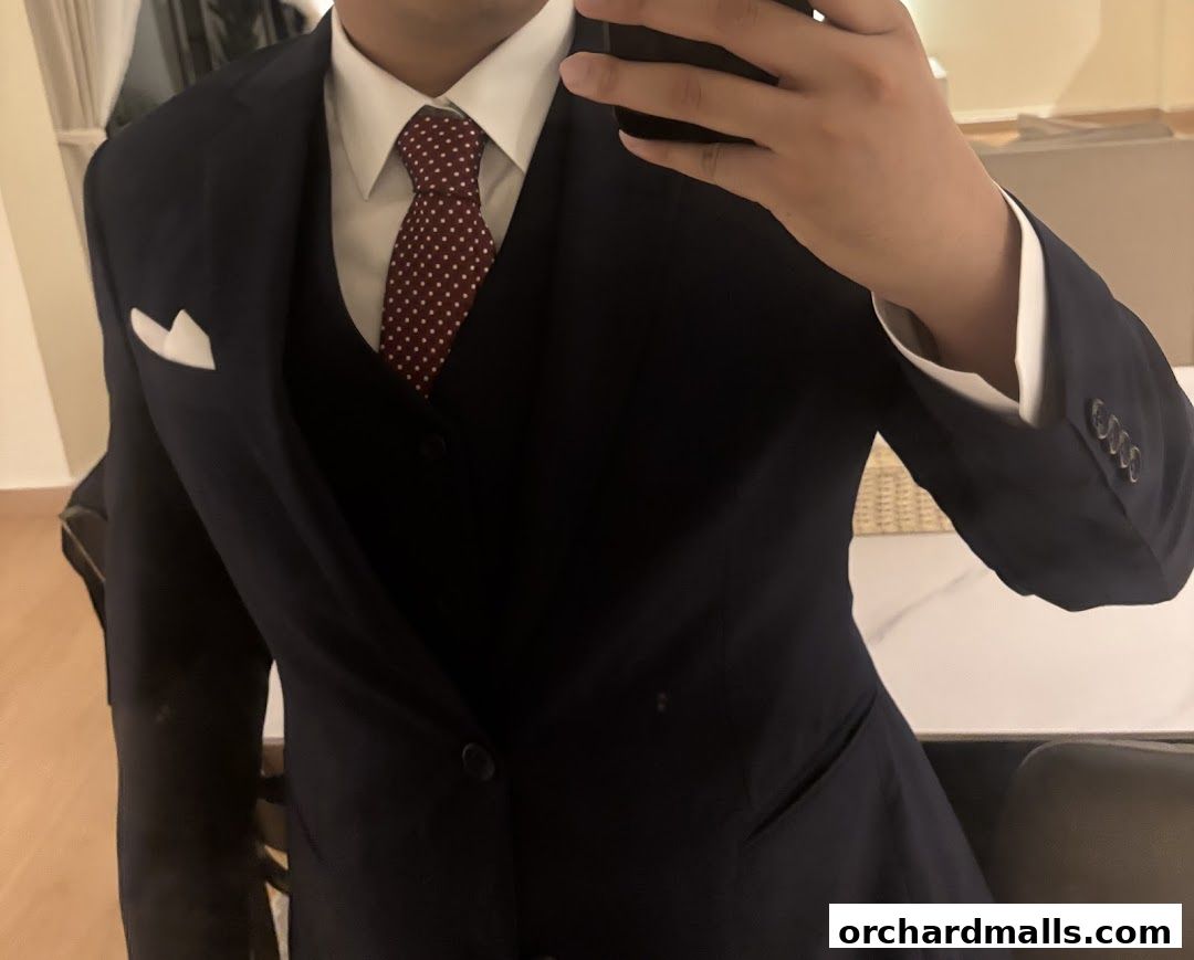 A person wearing a tailored navy blue suit with a white shirt and patterned tie.