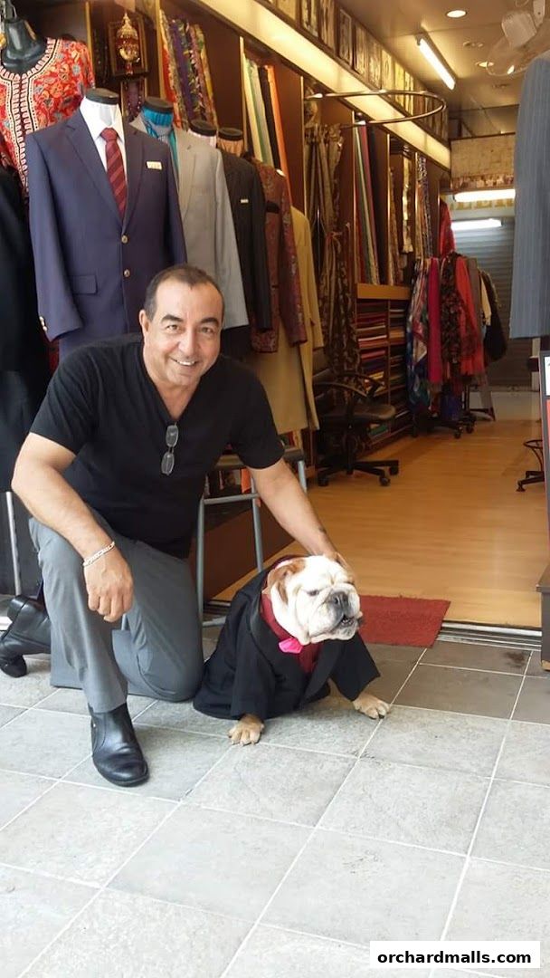 A man and a bulldog in a suit pose in front of a tailor shop.