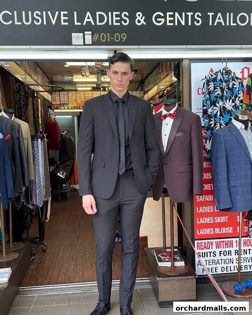 A man in a black suit stands in front of AP Custom Tailors, showcasing their tailoring services.