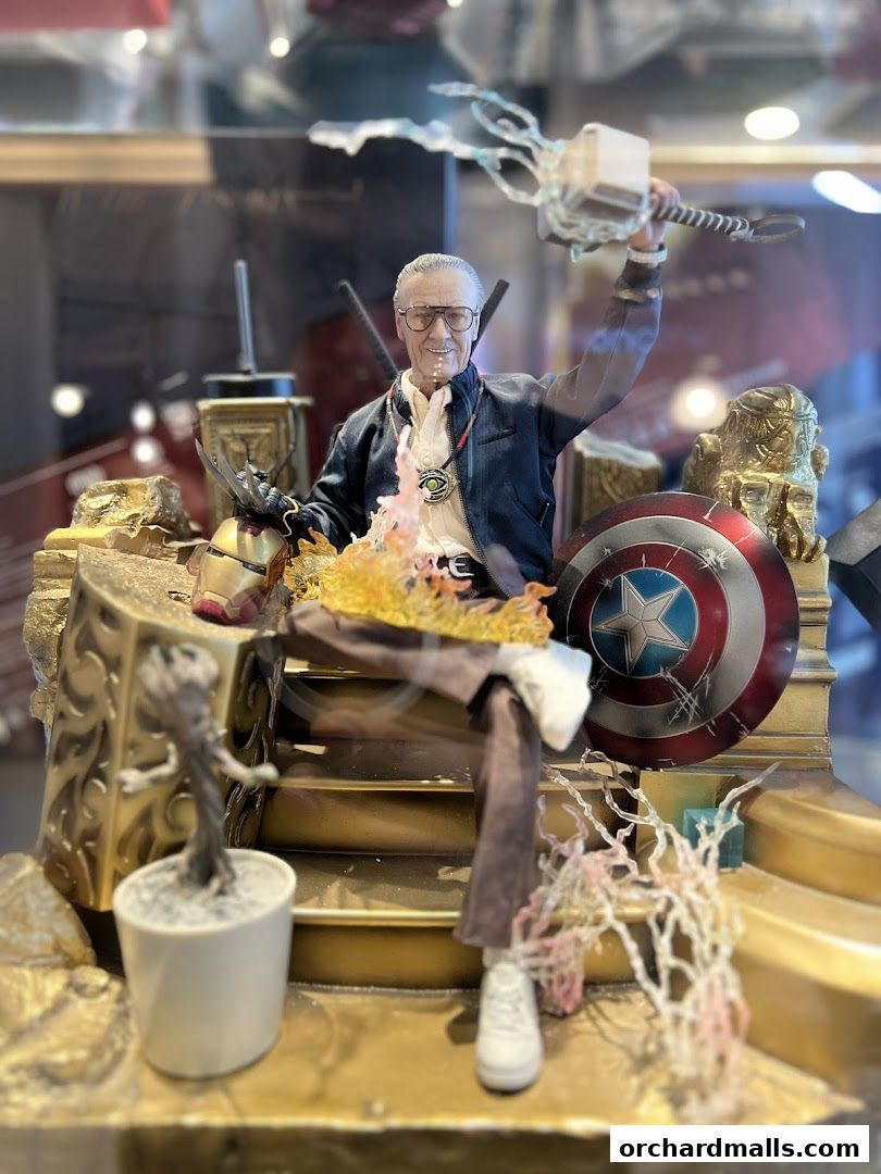 A detailed action figure of Stan Lee holding Thor's hammer and surrounded by Marvel memorabilia.
