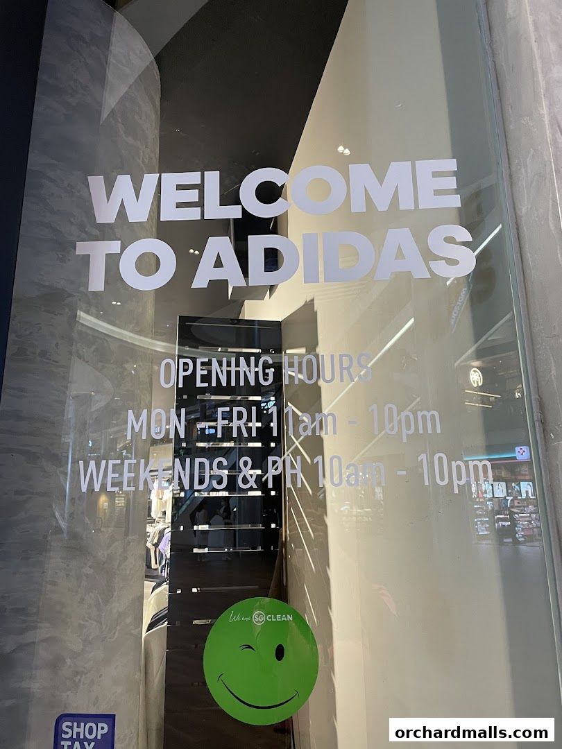 The entrance of an Adidas store with 'Welcome to Adidas' and opening hours displayed on the glass.