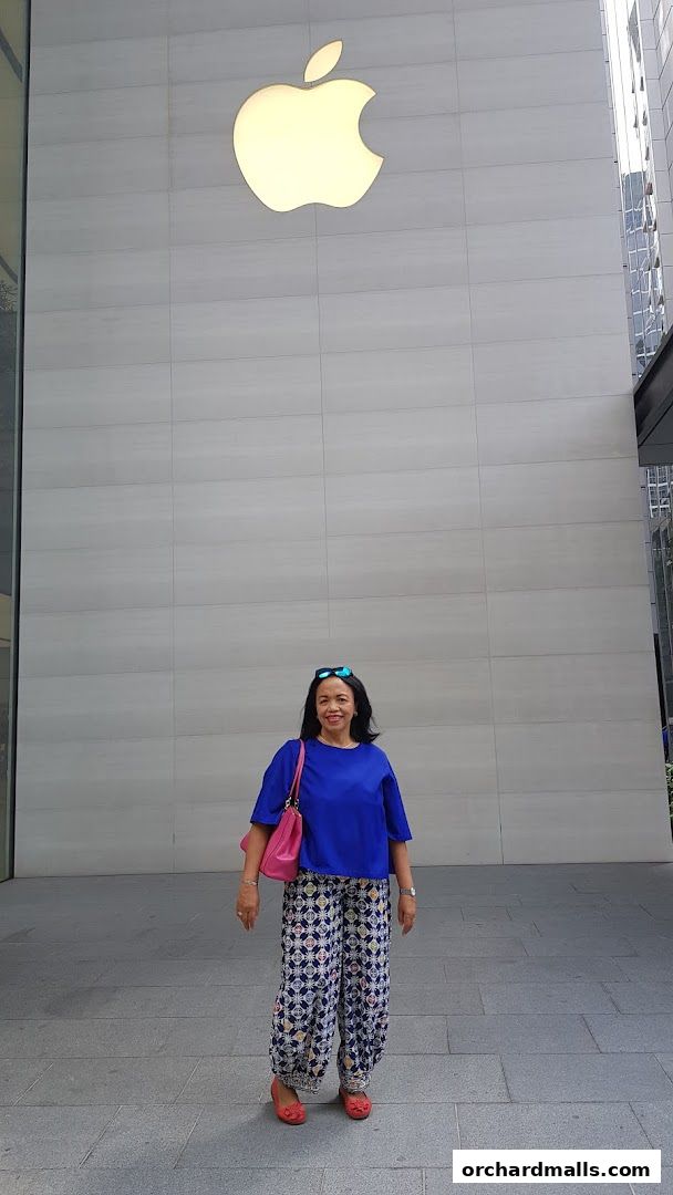 A woman stands in front of a large building with a prominent illuminated Apple logo.