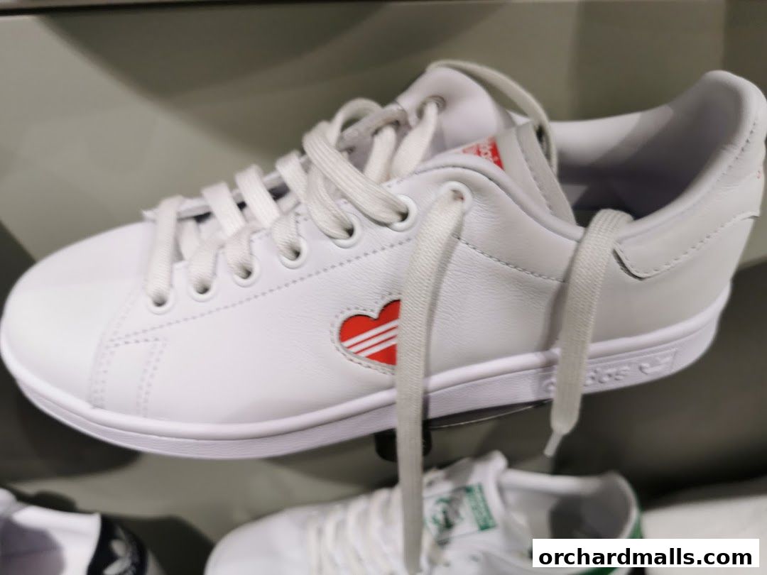 Close-up of a white Adidas sneaker with a red heart logo and white laces.