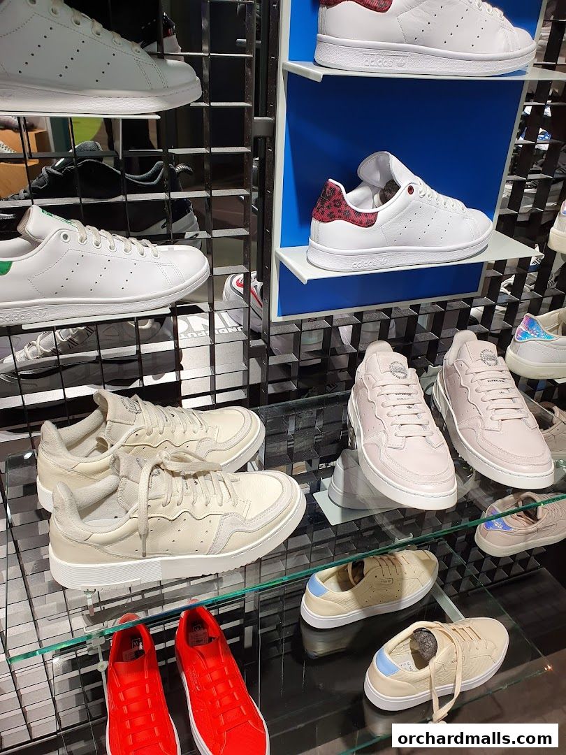 A display of various Adidas sneakers, including white, beige, pink, and red styles.