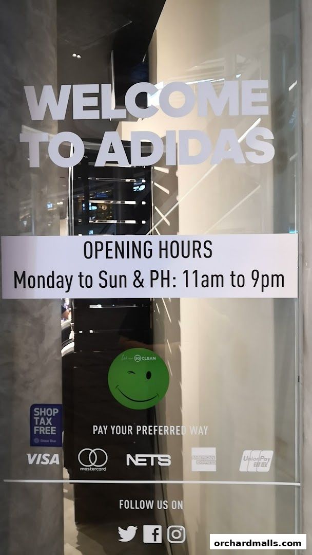 The entrance of an Adidas store with opening hours and payment options displayed on the glass.