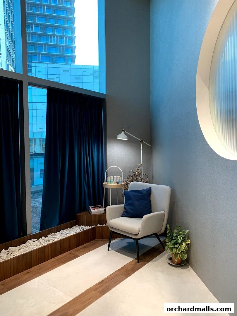 A comfortable waiting area with a chair, lamp, and plants, overlooking city buildings.