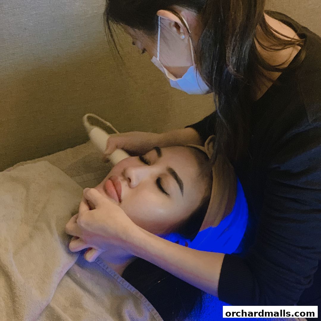 A beautician performs a facial treatment on a client with a device.