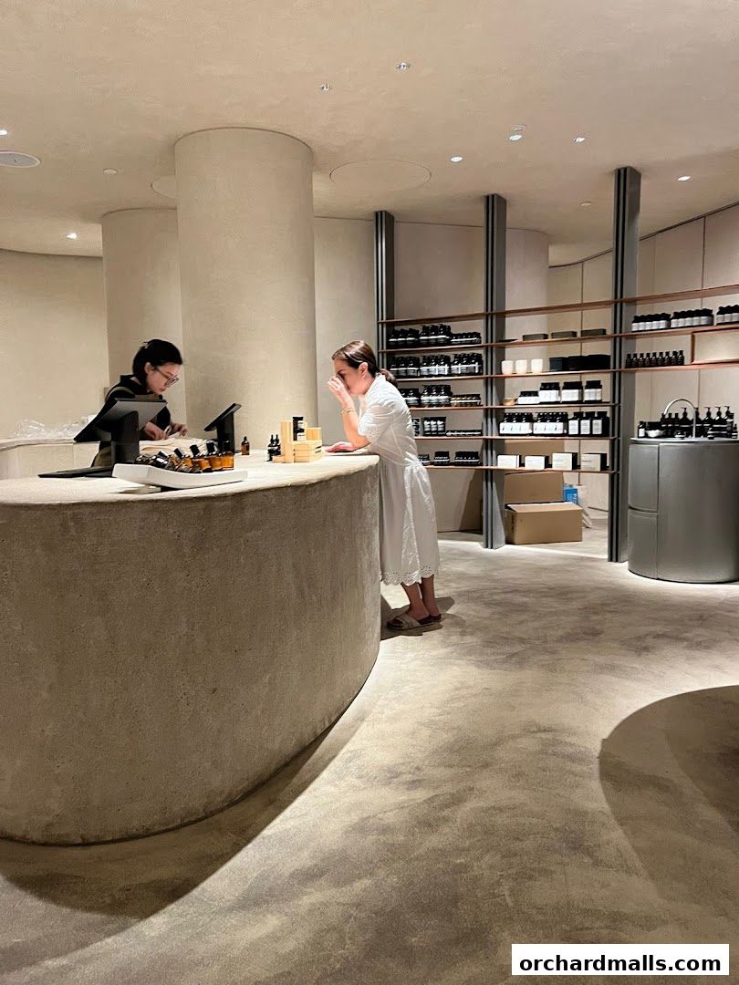 Customers interact with staff at the counter of a minimalist Aesop store.
