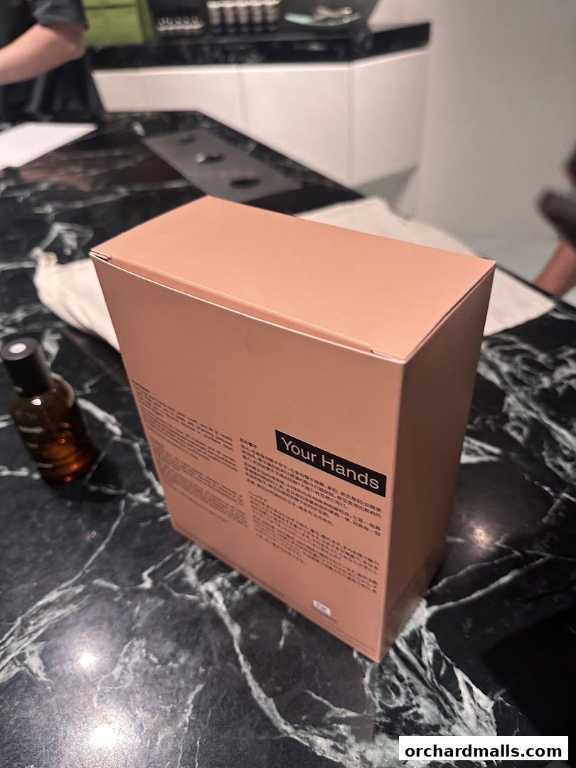 A peach-colored box labeled 'Your Hands' sits on a marble countertop next to a small amber bottle.