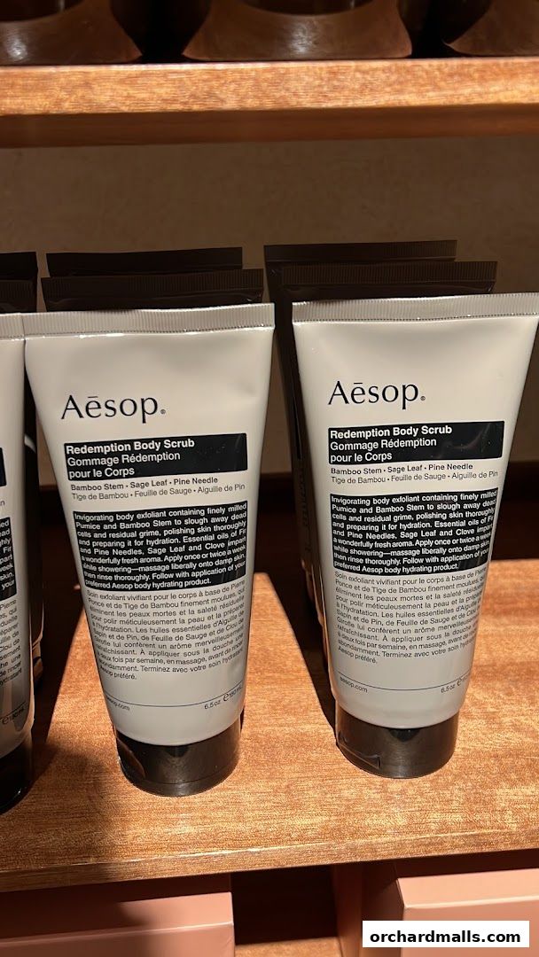 Two tubes of Aesop Redemption Body Scrub displayed on a wooden shelf.