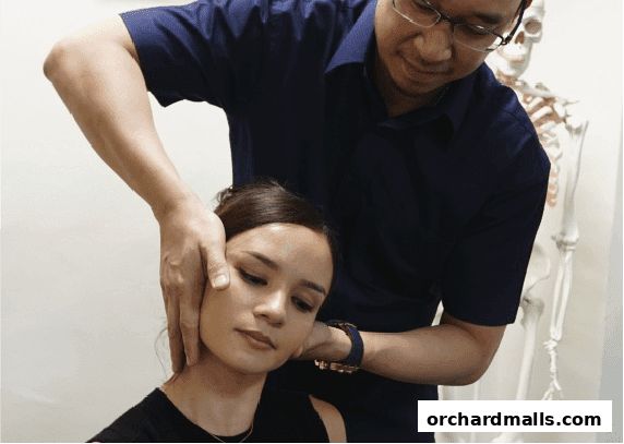A chiropractor adjusts a patient's neck, with a skeleton model in the background.
