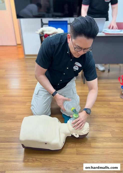 A man demonstrates CPR on a training dummy in a classroom setting.