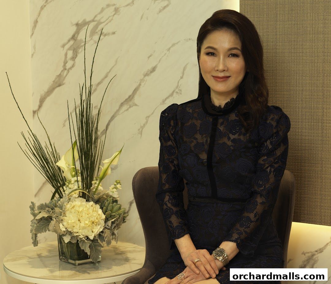 A woman in a navy lace dress sits next to a floral arrangement.