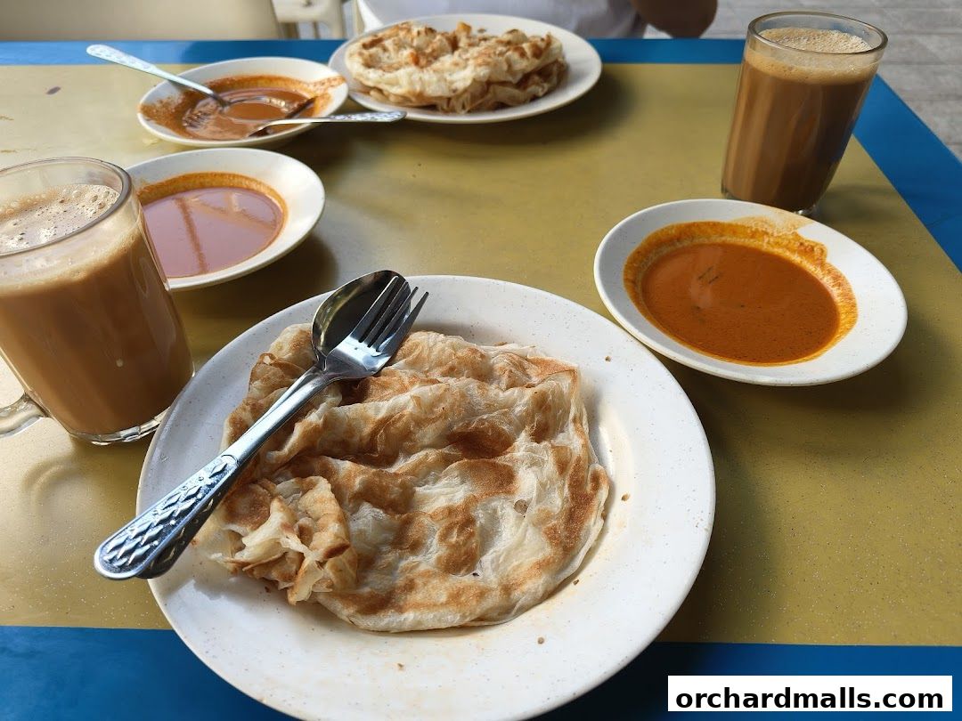 A close-up of Roti Canai with curry and a glass of Teh Tarik.