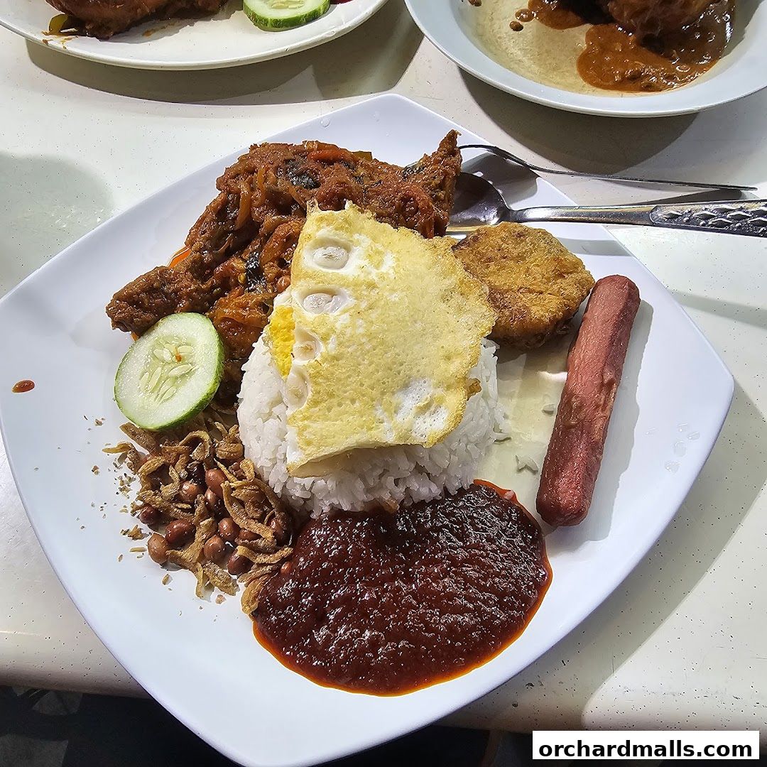 A plate of Nasi Lemak with fried chicken, fried egg, sausage, and sambal.