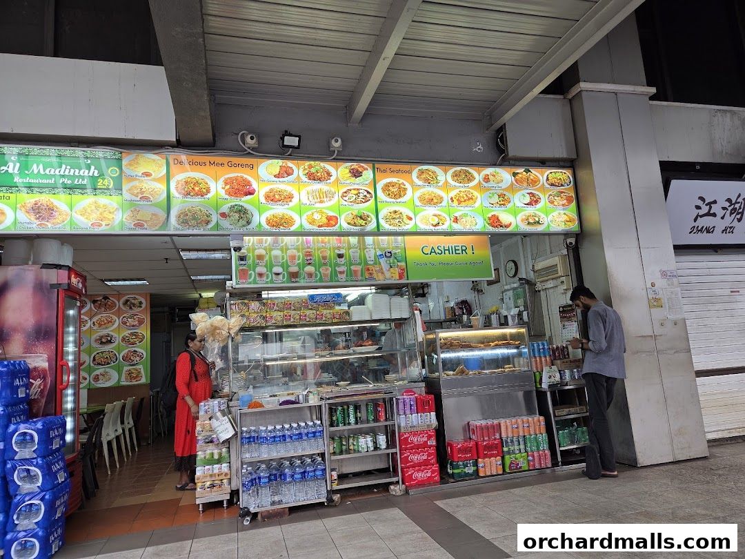 Exterior view of Al Madinah Restaurant with vibrant food displays and a cashier counter.