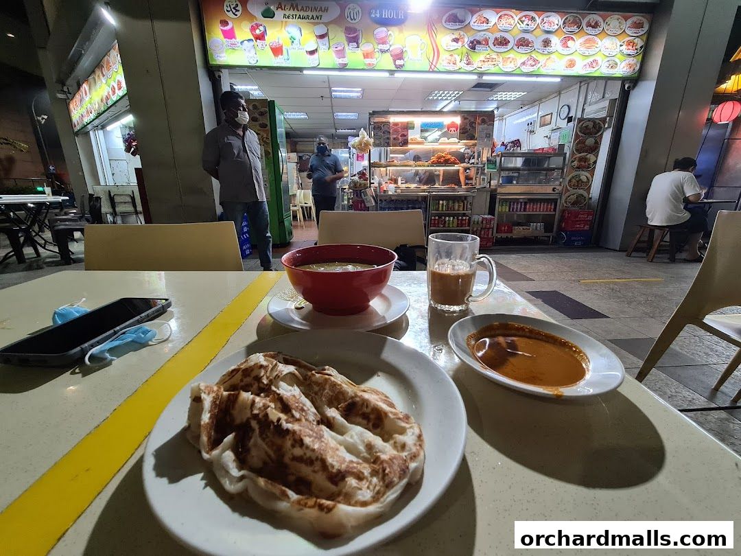 A table at Al Madinah Restaurant with food, drinks, and a phone.