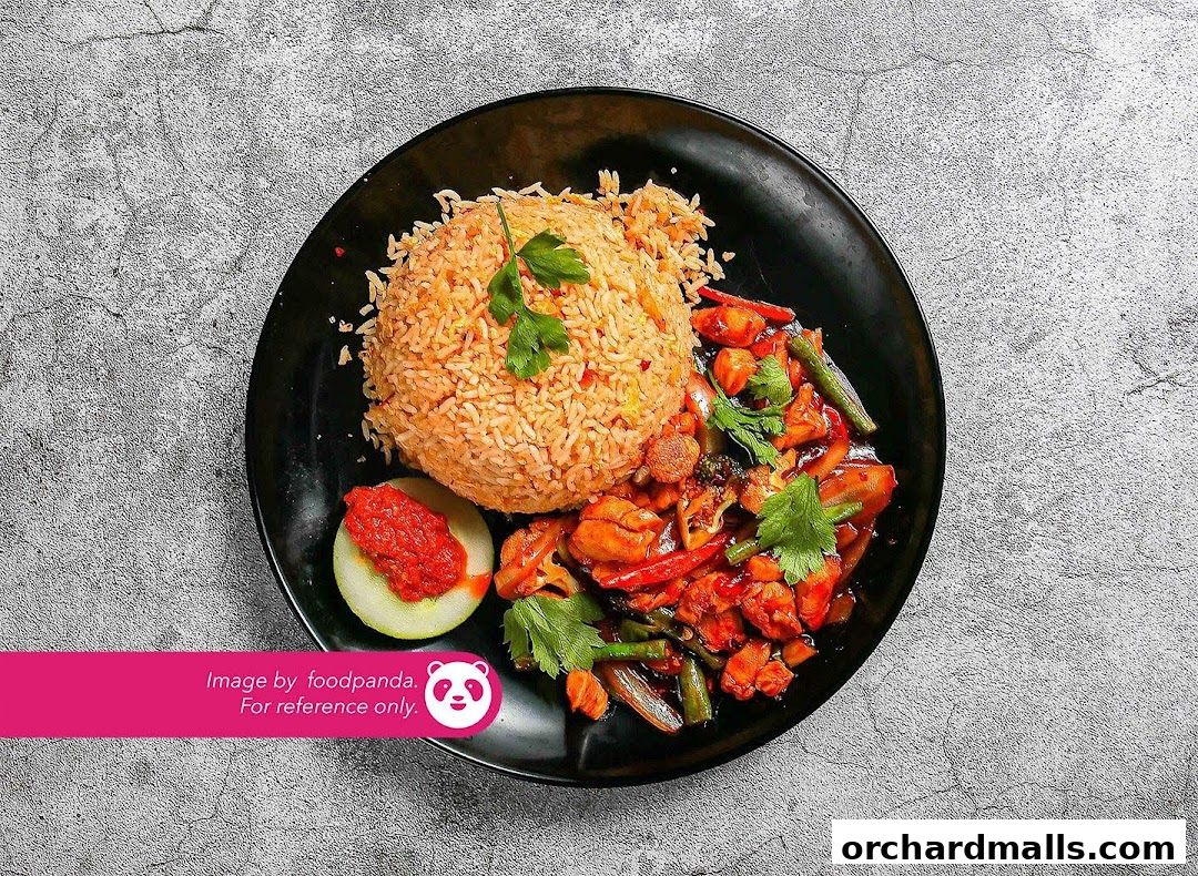 A plate of fried rice with chicken and vegetables, served with a slice of cucumber and chili paste.